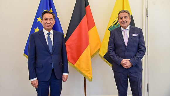 Das Foto zeigt den kasachischen Botschafter Dauren Karipov und Sachsen-Anhalts Landtagspräsidenten Dr. Gunnar Schellenberger vor Flaggen von EU, Bund und Land.