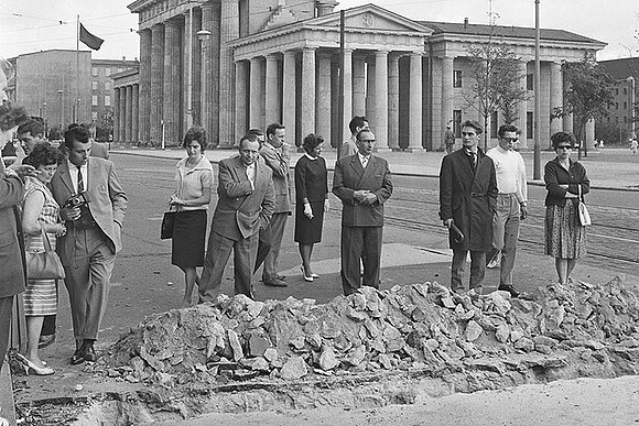 Historisches Foto: Passanten stehen vor dem aufgerissenen Straßenpflaster am Brandenburger Tor am 13. August 1961.