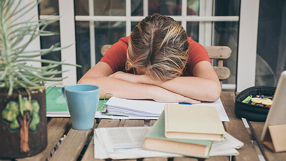 Fabio Principe - stock.adobe.com Kind sitzt erschöpft an Tisch über Schulbüchern