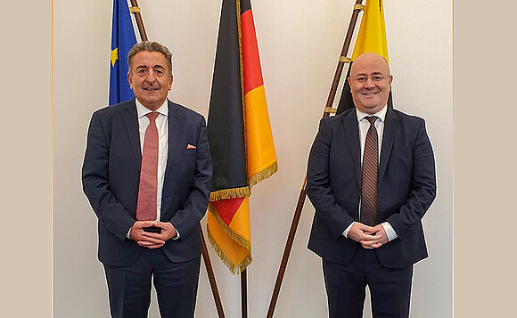 Präsident und Botschafter stehen vor Fahnen nebeneinander