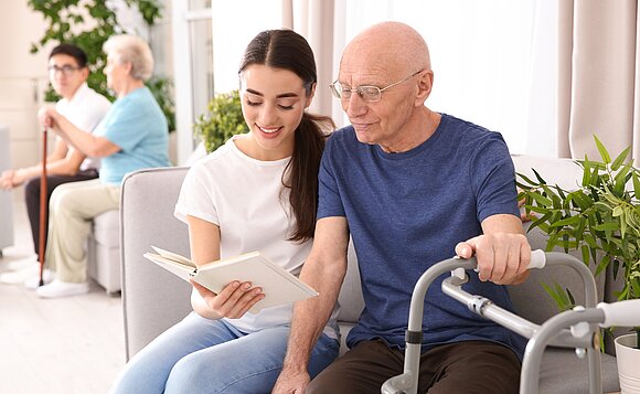 Ein Mädchen liest einem älteren Herrn etwas vor.