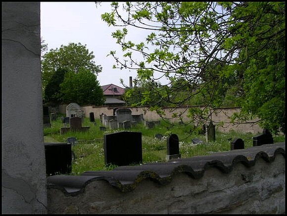 Blick über eine Mauer auf einen jüdischen Friedhof.