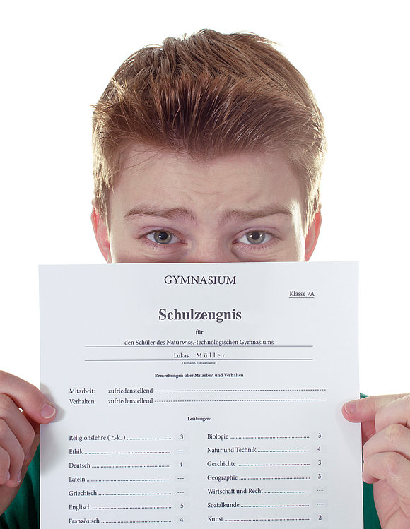 grafikplusfoto - stock.adobe.com Junge zeigt sein schlechtes Zeugnis in die Kamera und versteckt sich hinter den Papier.