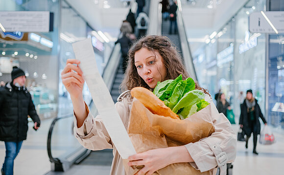 Die Verbraucherpreise steigen, ein deutliches Zeichen für die steigende Inflation. Symbolbild: Frau mit Kassenzettel und leerer Einkaufstüte.
