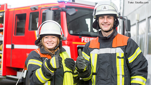 Feuerwehrfrau und Feuerwehrmann vor einem Einsatzwagen.