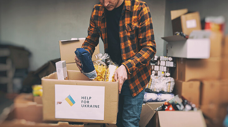 Ein Mann packt einen Karton mit Hilfsgütern. Die aus der Ukraine Geflüchteten werden auch in Deutschland aus der Zivilgesellschaft heraus mit Nahrungsmitteln und anderen Dingen des Alltags versorgt.