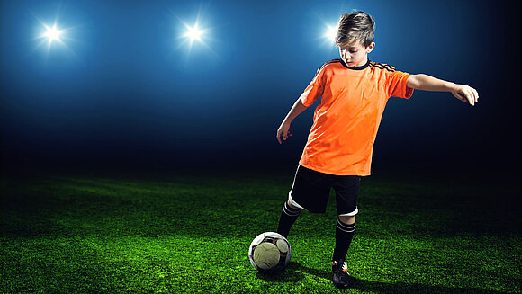 Ein Junge spielt unter Flutlicht Fußball.
