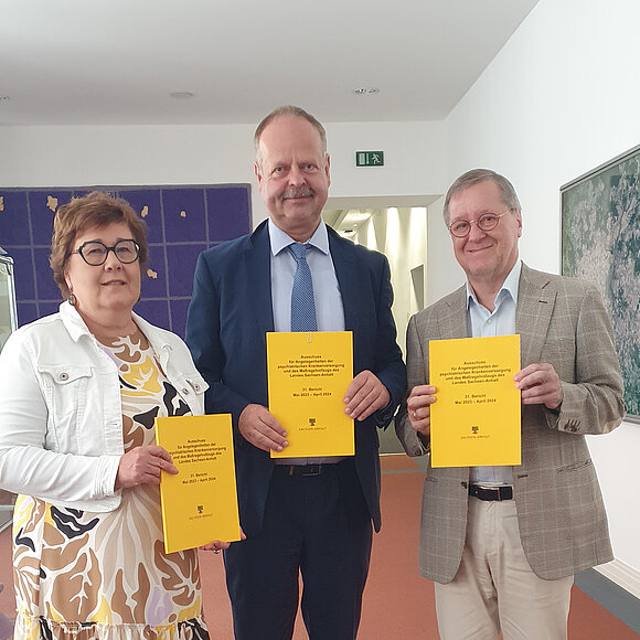 ltlsa/mau Drei Menschen stehen nebeneinander und halte einen gelben Bericht in die Kamera