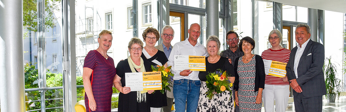 Menschen stehen mit Blumen und Spendenschecks in einer Reihe.