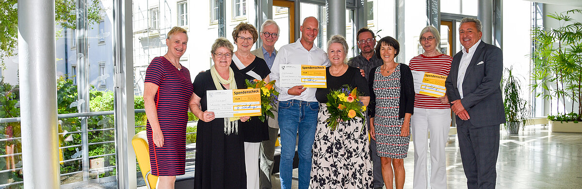 Menschen stehen mit Blumen und Spendenschecks in einer Reihe.