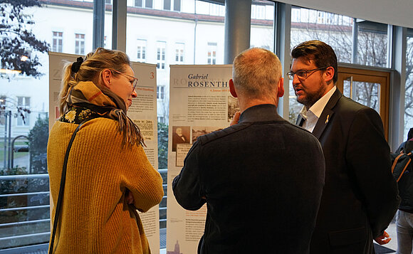 Besucher der Ausstellung stehen im Gespräch vor einer Ausstellungstafel