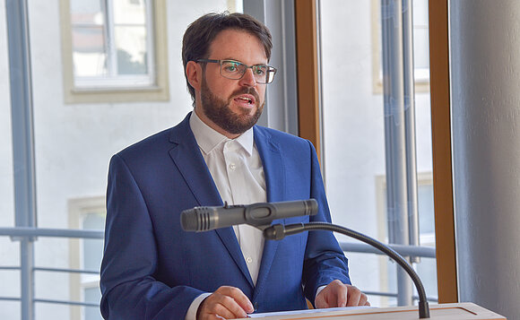 Daniel Grunow spricht am Rednerpult und führt in die Ausstellung ein.