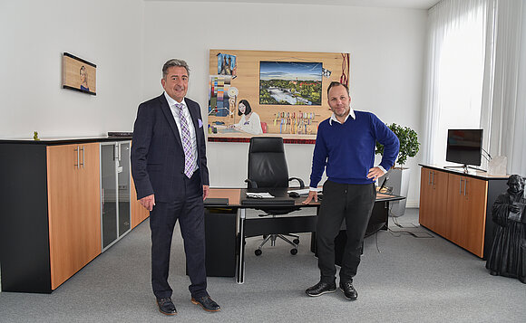 Landtagspräsident und Künstler stehen im Amtszimmer vor dem Bild, das an der Wand hängt.