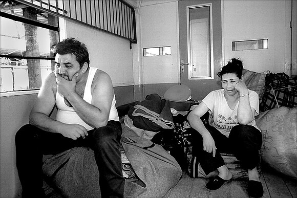 Knut Mueller Zwei Menschen (vertriebene Roma) sitzen auf wenigen Taschen im Bahnhof und warten.