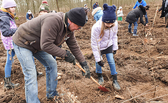 Ein Vater und seine Töchter pflanzen einen Baum.