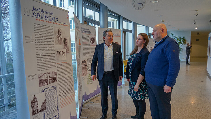 Drei Menschen stehen vor einer Ausstellungstafel und unterhalten sich