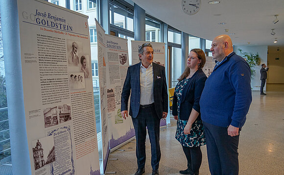 Drei Menschen stehen vor einer Ausstellungstafel und unterhalten sich