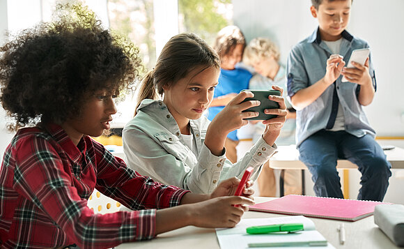 Kinder spielen mit ihren Smartphones oder schauen sich etwas an. Es ist Pause vom Unterricht im Klassenzimmer.