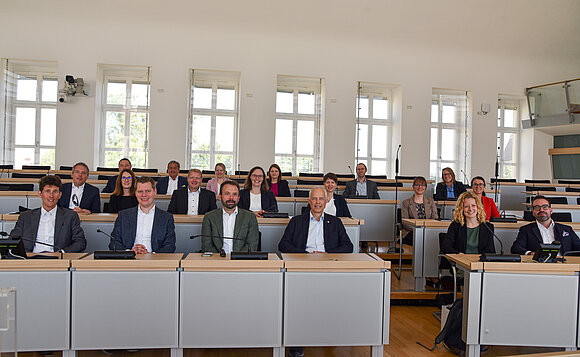 Menschen sitzen im Plenarsaal auf den Plätzen der Abgeordneten