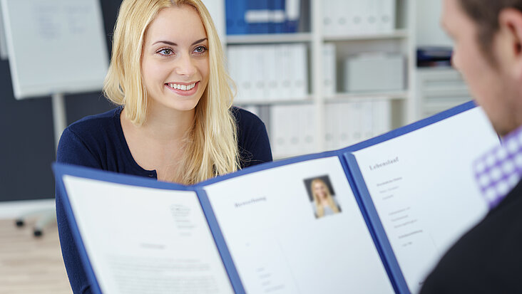 contrastwerkstatt/stock.adobe.com Junge Frau sitzt Personalchef gegenüber. Er blickt in ihre Bewerbungsmappe.