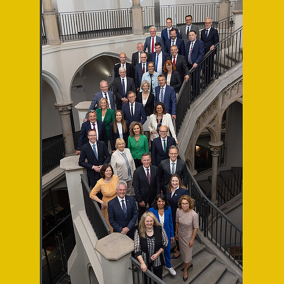 Präsidenten und Direktoren stehen auf Treppe und blicken in Kamera