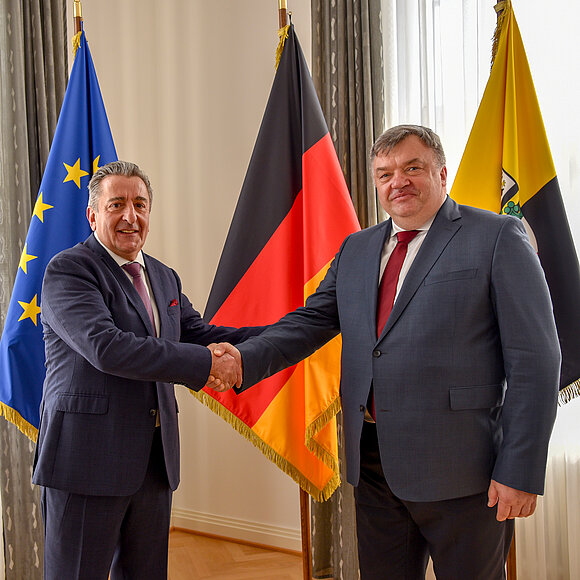 Shakehands von Landtagspräsident Dr. Gunnar Schellenberger und Litauens Botschafter Ramūnas Misiulis vor den Flaggen Europas, Deutschlands und Sachsen-Anhalts.