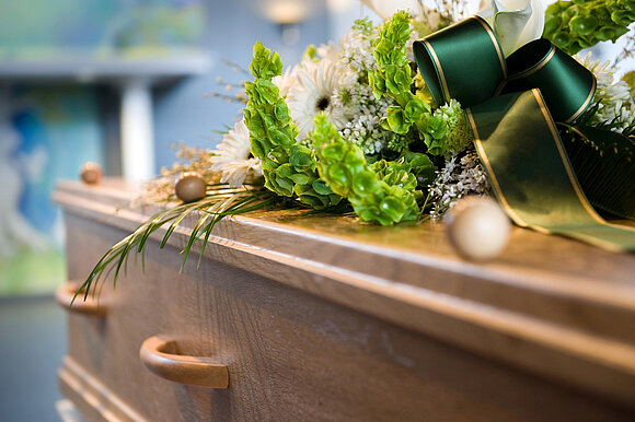Robert Hoetink – stock.adobe.com Ein Sarg mit Blumengesteck darauf