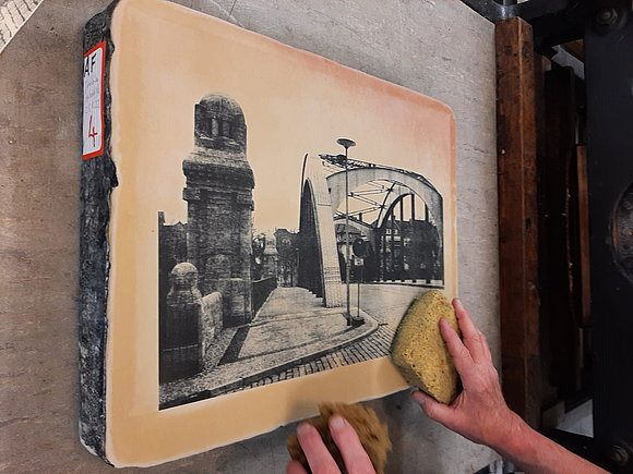 Eine Hand mit einem Schwamm fährt über ein gedrucktes Bild