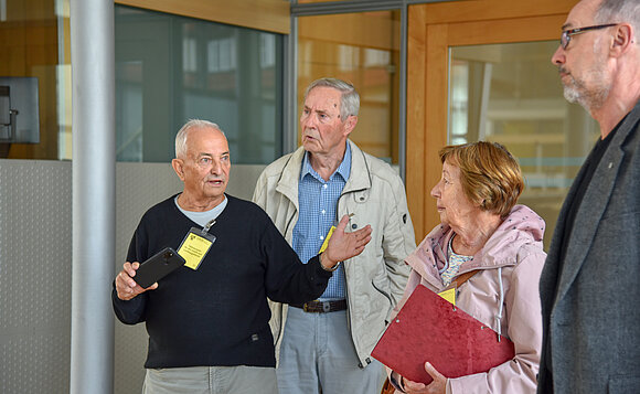 Vier Menschen stehen im Plenarsaal, einer erklärt den anderen etwas und gestikuliert dabei.