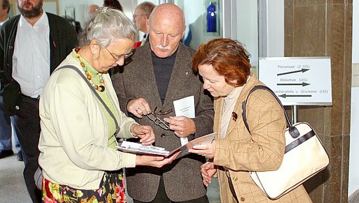 Besucher stecken ihre Köpfe zusammen und schauen in einen Flyer