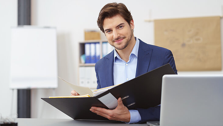 Seriöser Geschäftsmann arbeitet am Tisch sitzend im Büro und schaut in seien Unterlagen