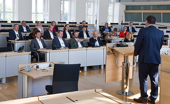 Menschen sitzen im Plenarsaal auf den Abgeordnetenplätzen