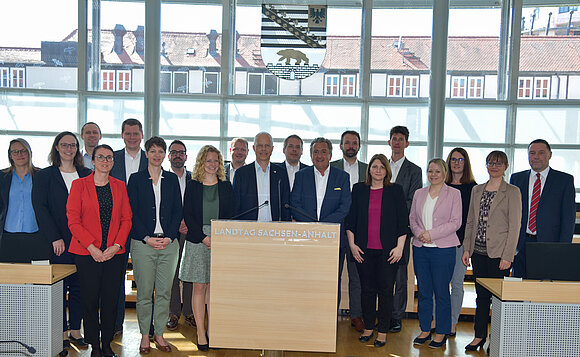 Gruppe steht im Plenarsaal vor dem Landeswappen