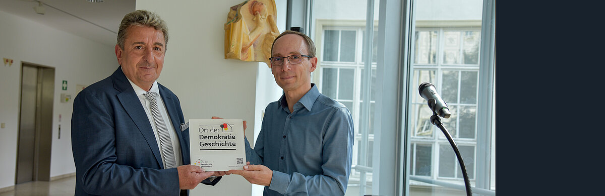 Zwei Männer halten gemeinsam eine Plakette in den Händen.