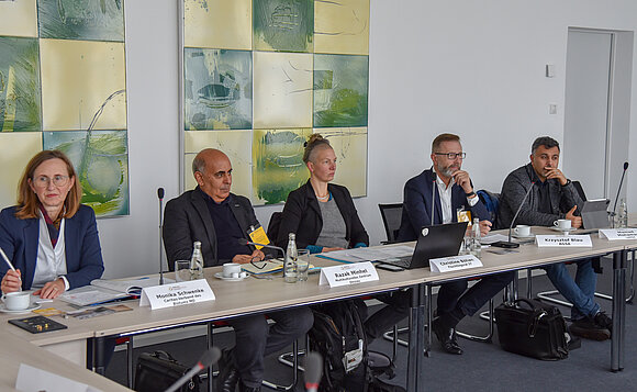 Fünf Mitglieder des Rundes Tisches sitzen an Tischen nebeneinander