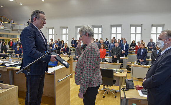 Die Vizepräsidentin des Verfassungsgerichts hebt vor dem Landtagspräsident die Hand zum Schwur. Daneben steht der Ministerpräsident
