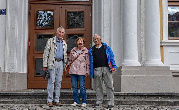 Drei Personen stehen vorm Landtagsgebäude und lächeln in die Kamera.