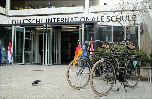 Blick auf die Deutsche Internationale Schule Den Haag, die im Rahmen der Delegationsreise besucht wird. Man sieht ein Eingangsportal und davor abgestellte Fahrräder.