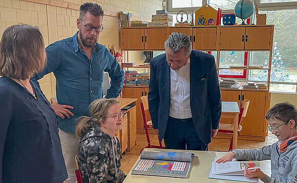 Landtagspräsident schaut zwei sitzenden Schülern beim Lernen über die Schultern.