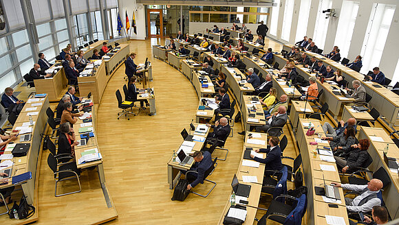 Blick von Besuchertribüne in den Plenarsaal, in dem Abgeordnete sitzen.