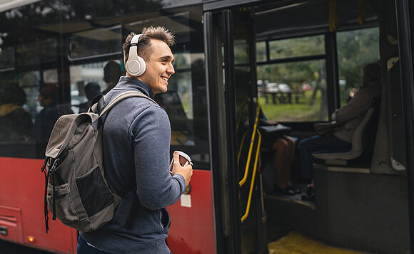 Ein junger Mann wartet vor einem stehenden Bus auf das Einsteigen.