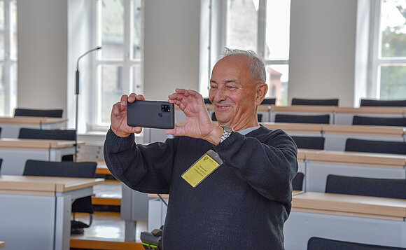 Ein Mann steht im Plenarsaal und fotografiert mit dem Handy.