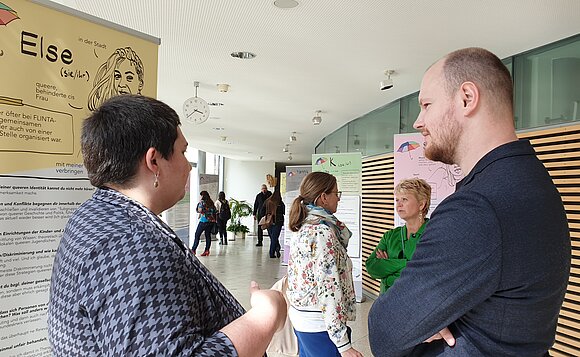 Gäste unterhalten sich vor den Ausstellungsplakaten.