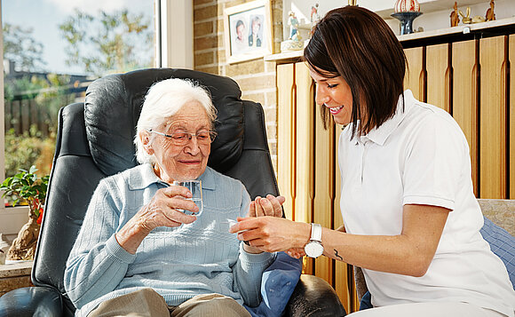 Eine Pflegehelferin geht einer Seniorin daheim zur Hand.