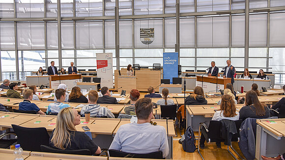 Blick in den Plenarsaal. An den Rednerpulten stehen die Verantwortlichen der Institutionen, die den Wettbewerb gemeinsam veranstalten.