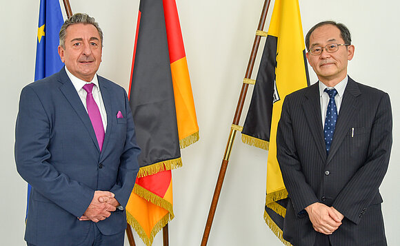 Landtagspräsident Dr. Gunnar Schellenberger und der japanische Botschafter Hidenao Yanagi posieren vor Fahnen.