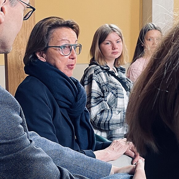 ltlsa/smü Eva Umlauf im Portrait, im Hintergrund Schülerinnen, die ihr zuhören.