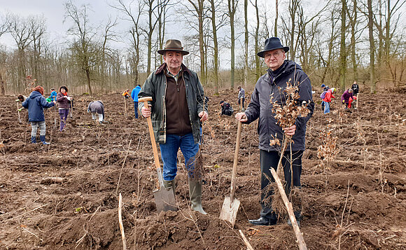 Auf einem Acker im Wald stehen der Landtags- und der Ministerpräsident mit Spaten in der Hand, um Bäume zu pflanzen.
