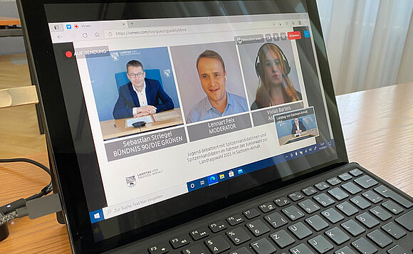 Blick auf einen Laptop während eines Livestreams. Zu sehen drei Personen, darunter der Abgeordnete Sebastian Striegel.