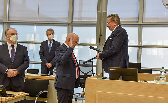 Der Präsident des Verfassungsgerichts hebt vor dem Landtagspräsident die Hand zum Schwur. Daneben steht der Ministerpräsident